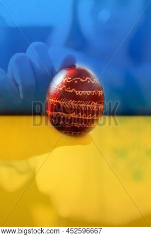 Defocus Ukrainian Girl In Vyshyvanka Holding One Colored Red Egg On Nature Background. Easter, Ukrai