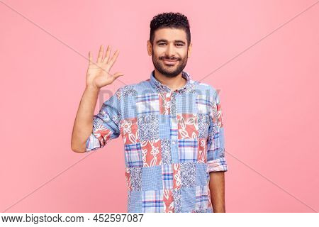 Hello, Welcome. Portrait Of Happy Young Adult Dark Haired Bearded Man In Blue Shirt Raising Palm To 
