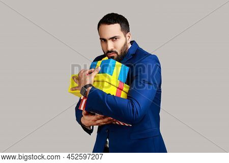 Portrait Of Angry Serious Bearded Man Holding Stack Of Presents In Hands, Being Greedy To Share Gift