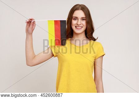 Portrait Of Pleasant Looking Teenager Girl In Yellow T-shirt Holding Germany Flag, Celebrating Day O