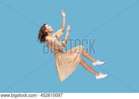 Hovering In Air. Relaxed Beautiful Girl In Yellow Dress And Curly Soaring Hair Levitating, Flying In
