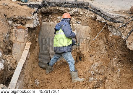 Man Dressed As Worker And Wearing Construction Helmet Is Digging A Large Hole With Shovel. Construct