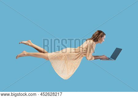Hovering In Air. Happy Cheerful Girl In Yellow Dress Levitating With Laptop, Typing Keyboard, Readin