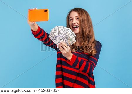 Excited Woman Wearing Striped Casual Style Sweater, Holds Smartphone In Hands And Broadcasting Lives