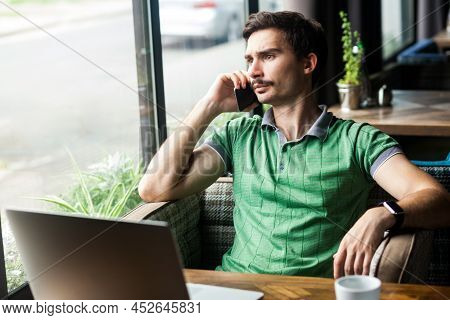 Portrait Of Man Freelancer Wearing Green T-shirt, Speaking Cell Phone, Discussing Problems, Looking 