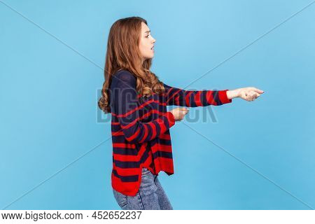 Side View Portrait Of Woman Wearing Striped Casual Style Sweater, Standing And Doing Pulling Gesture