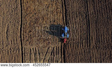 Tractor Driver On Tractor Plows Land. Aerial. Farmer In Tractor Plowing Ground