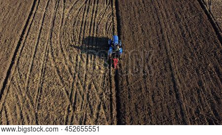 Tractor Driver On Tractor Plows Land. Aerial. Farmer In Tractor Plowing Ground