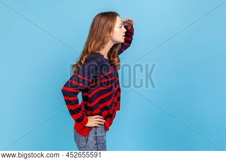 Side View Portrait Of Woman Wearing Striped Casual Style Sweater Keeps Hand Near Forehead Looks Far 
