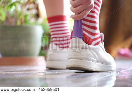 Man In Striped Socks Putting On White Sneakers With Shoehorn Closeup. Shoe Accessories Concept