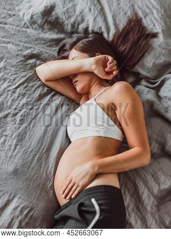 Tired pregnant woman sleeping on bed hiding face crying in depression or feeling morning sickness nausea. Mental health, fatigue, stress during pregnacy