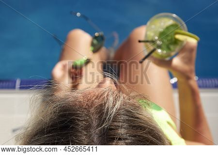 Close Up Photo From Above Of A Girl Sitting By The Pool, Enjoying A Cool Drink And Looking Into The 