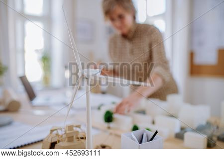 Senior Woman Eco Architect With Model Of Modern Bulidings Working In Office.