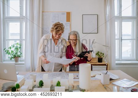 Mature Women Eco Architects With Model Of Modern Bulidings And Blueprints Working Together In Office