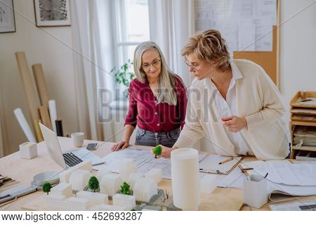 Mature Women Eco Architects With Model Of Modern Bulidings And Blueprints Working Together In Office