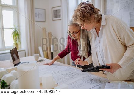 Mature Women Eco Architects With Model Of Modern Bulidings And Blueprints Working Together In Office