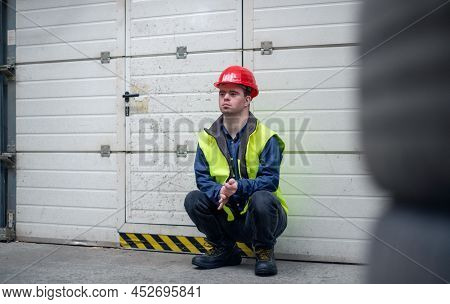 Young Man With Down Syndrome Resting When Working In Insutrial Factory, Social Integration Concept.
