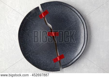 Broken Plate Is Red Taped Together On A Light Gray Concrete Table. Restoration Of Relations