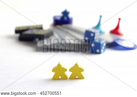 Two Yellow Wooden Meeple Game Pieces In Front Of Blurry Game Parts