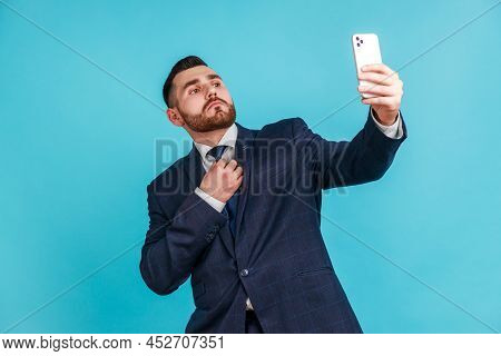 Portrait Of Self-confident Man With Beard Wearing Official Style Suit Straighten A Tie And Making Se