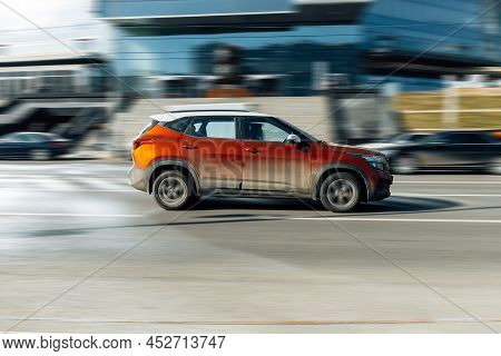Fast Moving Kia Seltos Crossover Rides On A City Road. Orange Color Car On Street In Motion. Overspe
