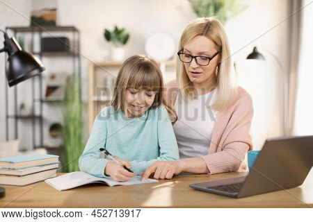 Caucasian Tutor Engaged With Schoolgirl Help Complete Tasks Sitting At Table At Home. Concept Of Edu