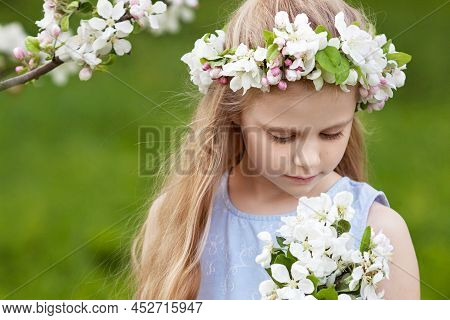 Beautiful Young Girl In Blue Dress In The Garden With Blosoming  Apple Trees. Cute Girl  Holding A B