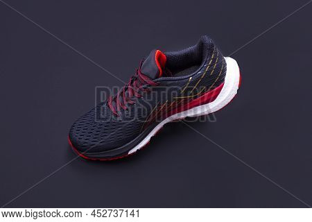 On A Black Background, A Black And Red Sneaker In Limbo. Sport Shoes. Sport And Healthy Lifestyle Co