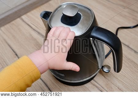 Toddler Baby Boy Holds A Hot Kettle With Boiling Water. Child Safety Issues In The Home Room, Little