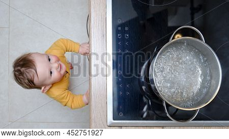 Toddler Baby Boy Looks At A Pot Of Boiling Water. Child Safety Issues In The Home Room, Little Kid