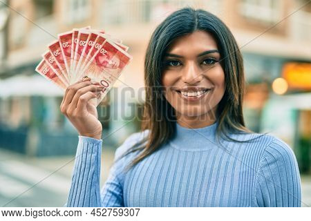 Beautiful hispanic woman smiling confient holding 20 shekels banknotes at the city