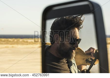 Reflected View Of Bearded Man Carrying Skateboard In Car Mirror. Mature Man In Sunglasses Standing O
