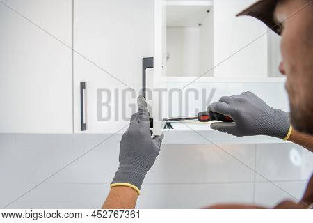 Cabinetmaker Contractor Worker Assembling White And Modern Kitchen Cabinets Inside An Apartment.