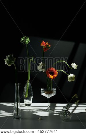 Vertical Modern Still Life Composition Of Various Fresh Flowers In Transparent Glass Vases And Coupe