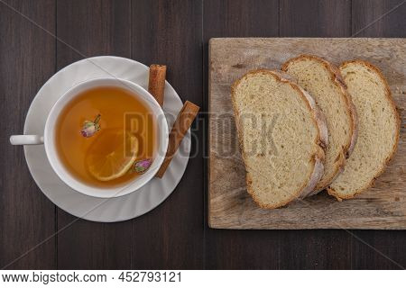 Top View Of Cup Of Hot Toddy With Lemon Flower Inside And Cinnamon On Saucer With Sliced Crusty Brea