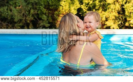 Teaching To Swimming. Mother With A Her Lettle Daughter Swimming In The Pool. Back View. Summertime.