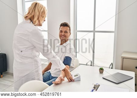 Middle age man and woman doctor and patient using tensiometer having medical consultation at clinic