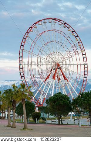 Close-up Of The Ferris Wheel Against The Background Of Snow-capped Mountains. Beautiful City Landsca