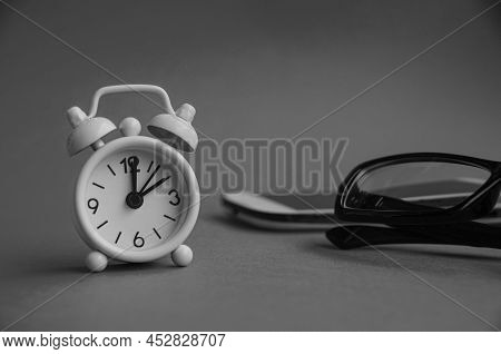 Alarm Clock Pointing At 2 O'clock With Glasses, Phone And Black And White Background. Copy Space