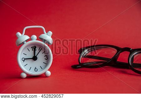 Alarm Clock Pointing At 9 O'clock With Glasses And Red Background. Copy Space