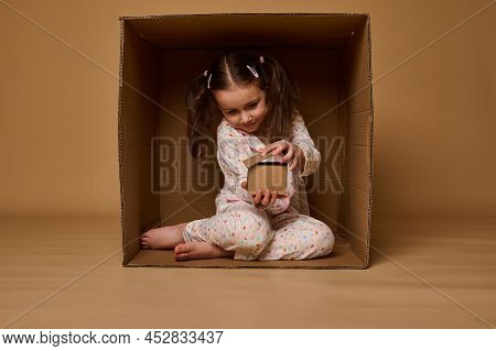 Adorable Caucasian Child Girl Hiding Inside A Box And Playing With A Craft Cardboard House Model. Re