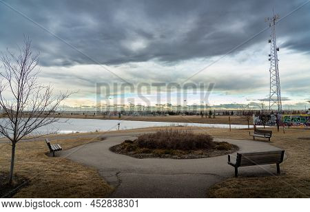 Airdrie Alberta Canada, April 04 2022: A Frozen Storm Water Retention Pond And Park Benches At An Of