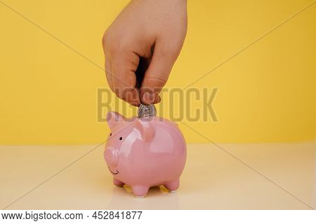 Hand Is Putting Coin Into Piggy Bank. Saving Money Concept