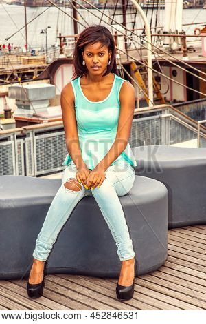 African American Woman Traveling In New York, Wearing Green Tank Top, Blue Fashionable Jeans, Sittin