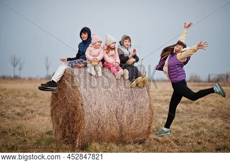 Four Kids With Mother Having Fun On Haycock At Field.