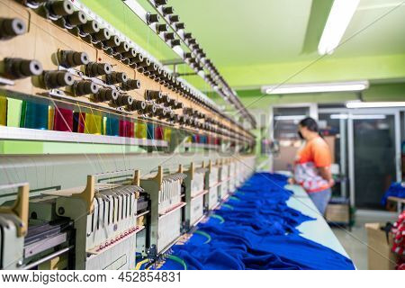 A Worker Stands In Control Of A Sewing Machine. Embroidery Area In Textile Factory In Industrial Zon