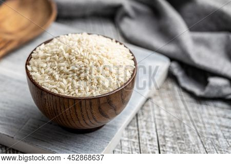Uncooked Carnaroli risotto rice in bowl on a wooden table.
