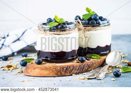 Parfait With Blueberry, Granola And Jam In Two Glass Jars At Light Background. Healthy Dessert Or Sn