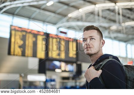 Man With Backapack At Airport. Portrait Of Tourist Against Arrival And Departure Board.