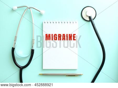 On A Blue Background, A Stethoscope And A White Notepad With The Words Migraine. Medical Concept